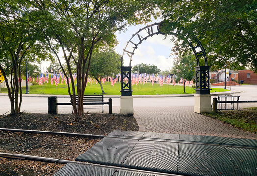 View from the wooded waterfront Conway Riverwalk looking towards a small park with a display of multiple American Flags in the small town of Conway, South Carolina.