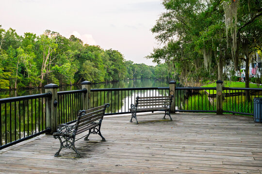 A wide wooden deck with benches along the waterfront boardwalk at the Waccamaw River Conway Riverwalk in the small town of Conway, South Carolina in the Southeast USA.