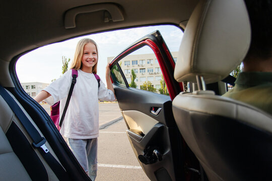 Happy girl opening back door of family car and smiling during afternoon school pickup, showing loving everyday family routine