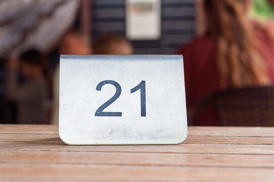 Metal table number 21 on a wooden table in a restaurant setting with blurred background people