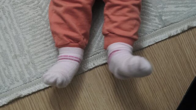Close-up top view of baby feet wearing pink socks kicking playfully on carpeted floor