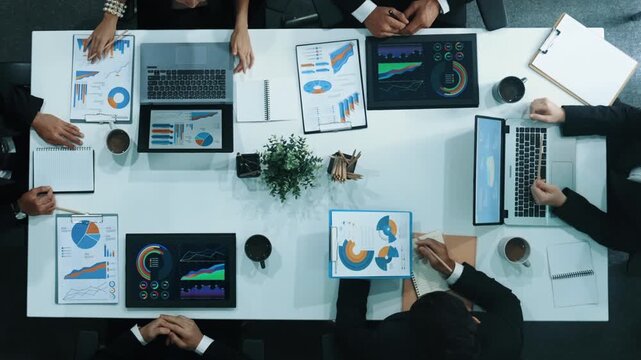 Top down aerial view of business people discussing about financial strategy on table with document and tablet display investment statistic at meeting. Diverse team brainstorm about plan. Directorate.
