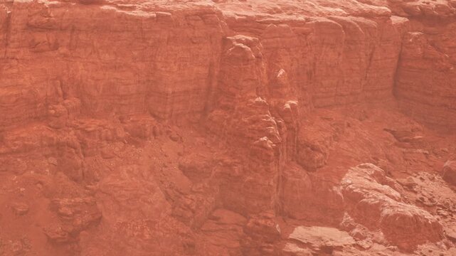 The scene shows a vast expanse of rocky terrain in shades of red. The canyon walls rise steeply, with natural formations scattered throughout. The sunlight casts shadows.