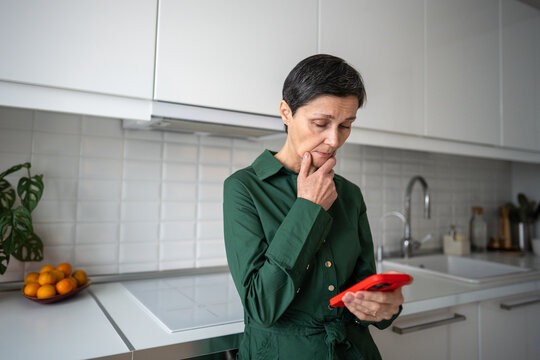 Pensive worried mature woman receiving bad news from smartphone message at home. Emotional shock, digital communication, personal crisis, mental distress, isolation, life disruption, female despair 