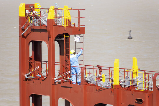 Maritime crew member inspecting container lashing equipment during final preparations for a new ship's maiden voyage.