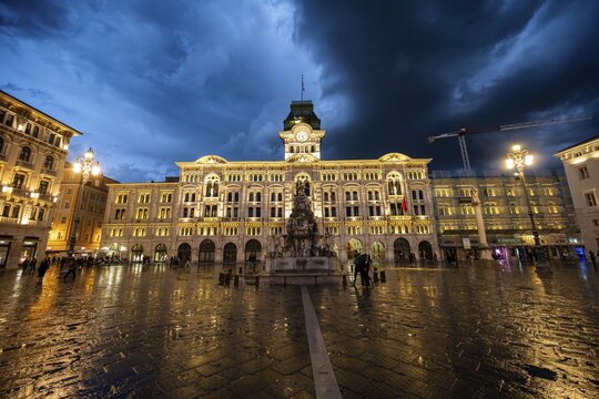 Illuminated square Piazza Unit&agrave; d'Italia, Town Hall, Palazzo Communale, with reflection, dramatic clouds, blue hour, old town, Trieste, Friuli-Venezia Giulia region, Italy