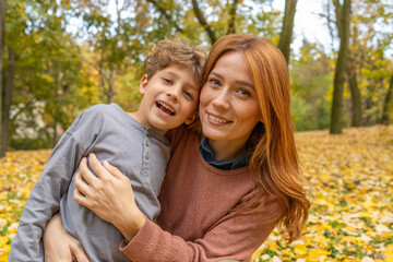 Fototapeta premium Mother and son embracing in a park during autumn with fallen leaves