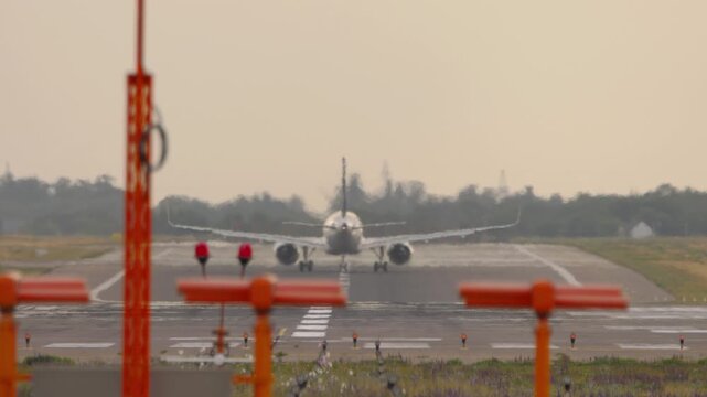 Airplane taking off from airport runway ascending into sky, back view with heat haze distortion and runway navigation lights.
