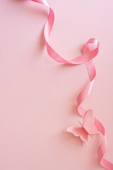 Fototapeta premium Pink ribbon and paper butterfly on soft vertical pink background for Breast Cancer Awareness Month support and hope