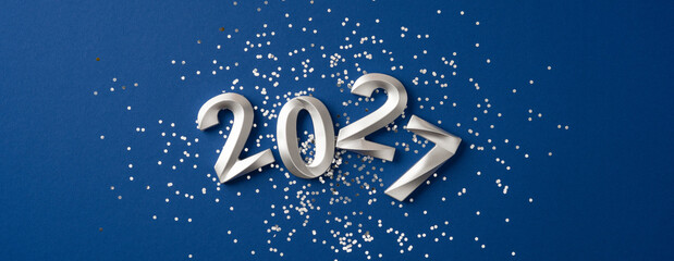 Naklejka premium Happy New Year 2027 celebration with silver numbers and confetti on blue banner background