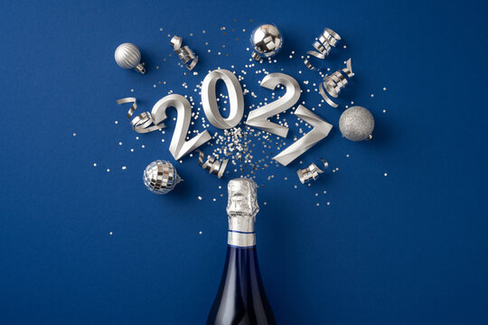 Happy New Year 2027 celebration with champagne, silver confetti and holiday ornament on blue