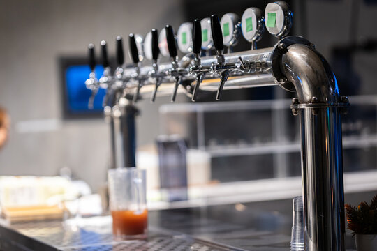 multi-tap draft beer dispenser system made of stainless steel, mounted on a pub counter. Featuring multiple chrome spigots for serving craft beer and draft beverages in a modern bar environment.
