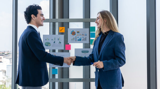 Two businessman and businesswoman partners shaking hands in suits standing Talking Discussing presenting financial graph Concept business expressed embolden and successful concept in the meeting room