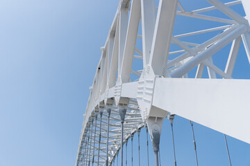 White steel bridge curves gracefully against clear blue sky. Strong structural beams form elegant, geometric pattern. Modern engineering meets natural sky in striking contrast. Ideal for architecture © Rizky Rahmat Hidayat