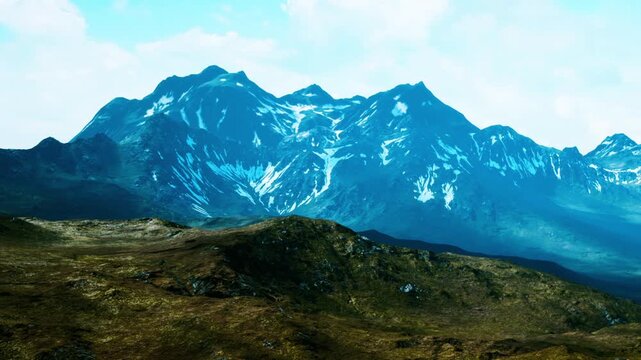 Snow capped mountains rise high against a blue sky. The landscape is rugged with patches of green. This scene captures natures beauty in a remote area during daylight.