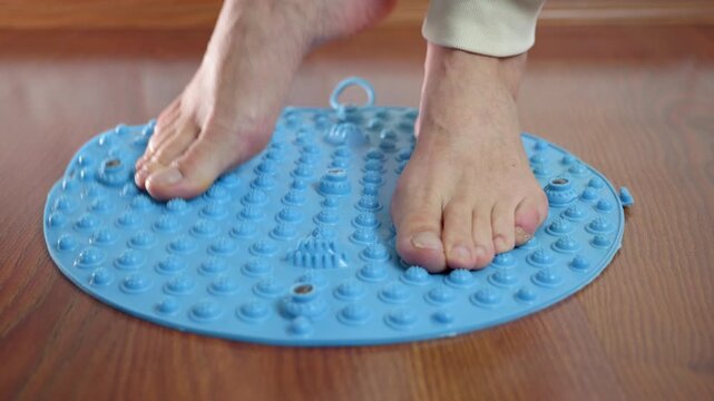Person using a foot massage mat for reflexology and acupressure therapy. Barefoot person standing on a blue spiked plastic mat, performing self-massage exercises for foot pain relief