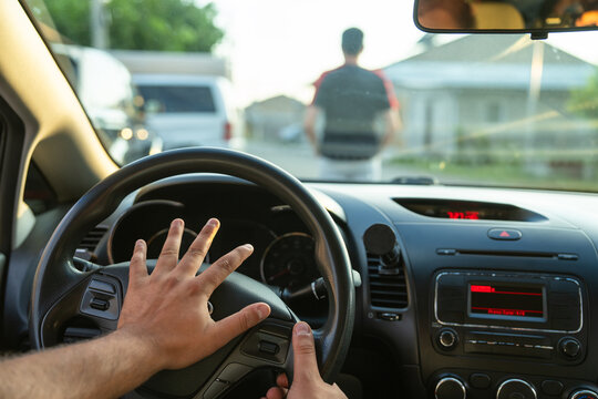 The driver honks to warn the pedestrian because the pedestrian is walking in the wrong direction from the car, creating an emergency.