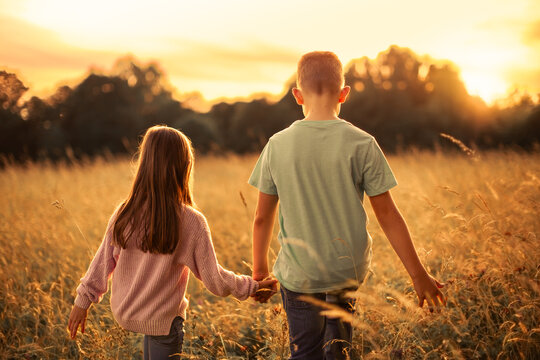 Loving caring Brother and Sister Holding Hands Walking Through Golden Meadow at Sunset, family children siblings bonding 