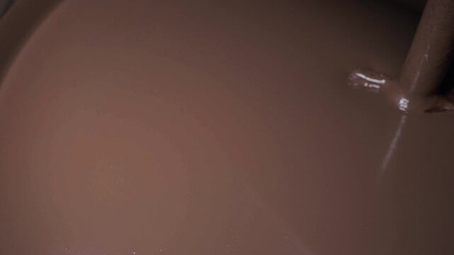 Close-up of melted liquid chocolate pouring over confectionery candies on automated conveyor belt in factory