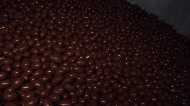 Close-up of melted liquid chocolate pouring over confectionery candies on automated conveyor belt in factory