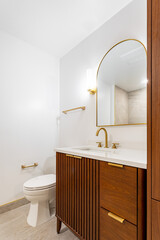 Modern bathroom interior with wood vanity, arched mirror, gold fixtures and white countertop