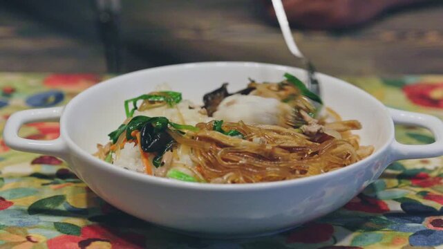 Homemade Korean Japchae Rice 02 - with Spoon.
A spoon mixing and scooping up delicious homemade Korean glass noodle rice (Japchae-bap) from a white porcelain bowl. Appetizing home-cooked meal b-roll f