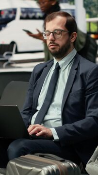 Vertical screen: Frustrated business traveler works on laptop in bus station