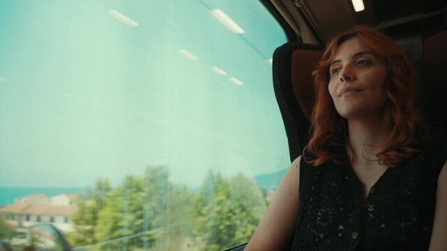 A woman looks out the window of a train while traveling near the sea in summer