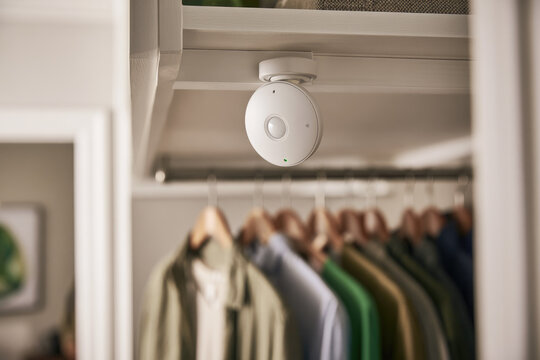 Ultra slim magnetic motion sensor installed beneath wardrobe shelf, with subtle indicator light above hanging clothing in bright contemporary closet interior for energy saving security