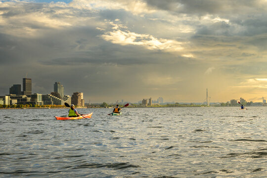 Three sea kayakers paddling on Toronto's Inner Harbour under dramatic morning clouds, with copy space in the sky