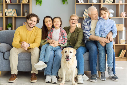 Family grandparents parents children dog together at home. Three generations sitting with labrador, smiling at camera in living room portrait. Clear concept family love across generations.
