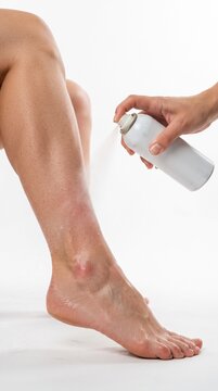Applying foot spray to a leg with tanned skin. The person's skin is smooth, and the spray is creating a mist around the lower leg and ankle