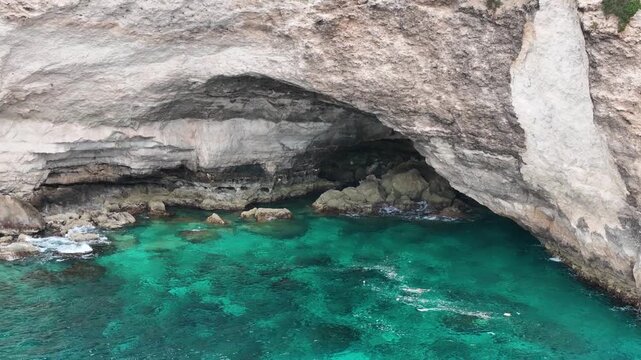 sea arch frames a calm turquoise cove limestone archway aerial drone orbit malta coastline rock formation submerged rocks clear water coastal erosion secluded inlet mediterranean