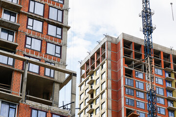 Residential buildings under construction with exposed concrete structures and tower crane, showing urban development, real estate growth and modern construction processes © belavinstock