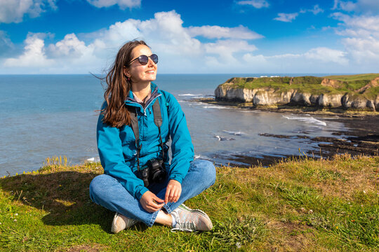 Happy female hiker resting on coastal trail above chalk cliffs in Flamborough, England, UK