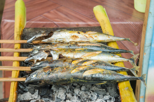 Delicious silver fish seasoned with spices being grilled on an open charcoal barbecue grill. Outdoor cooking of healthy seafood with a rustic wood grain background during daytime.