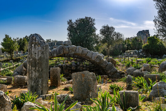 Weathered megalithic blocks. The archaeological site is surrounded by lush green agave plants and Mediterranean trees, highlighting the connection between nature and history. Turkey, Mersin.