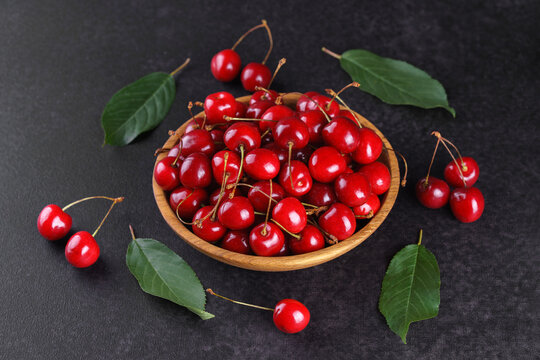 Fresh ripe sweet cherries in rustic wooden bowl on black stone textured background with copy space for text. Juicy organic summer fruit, red berries, healthy seasonal food, farm harvest