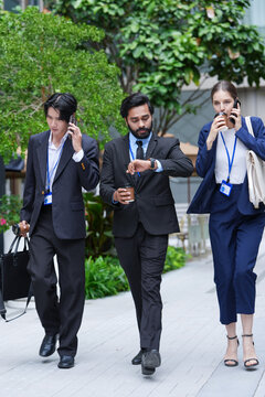 A multiethnic business team of three colleagues walk through the district checking their smartphones outside a glass office tower in a modern Asian financial (frame 193)