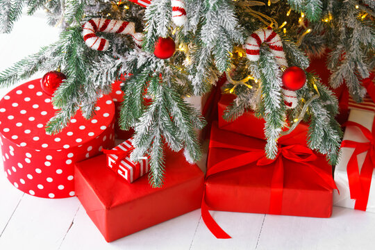 Beautiful presents, gift boxes wrapped in elegant red paper under green snowy festive Christmas tree with warm lights. Cozy winter holiday atmosphere perfect for seasonal celebrations and decor themes