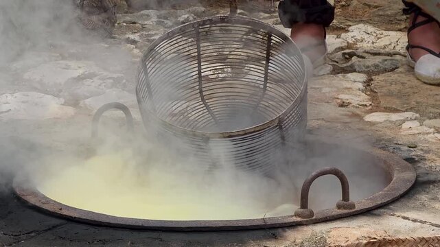 Adding lye potash mixture into boiling kettle water and dipping fresh grapes in metal basket during traditional escalda process.