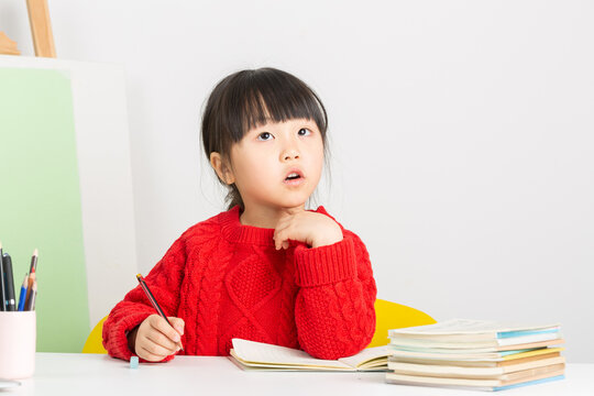 A bright and focused Asian girl is doing her homework at her desk, her expression one of deep thought.