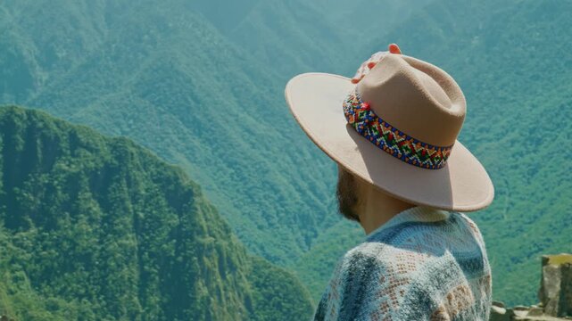 Adult man in ethnic hat looking at lush green mountain landscape, travel and contemplation concept