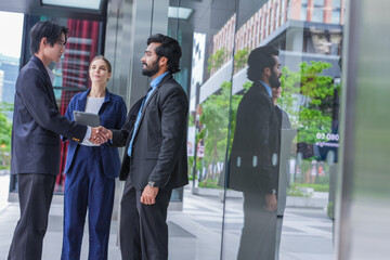 Fototapeta premium An Asian businessman, an Indian businessman and a European businesswoman return to the office after a successful handshake on a landscaped city plaza surrounded by high rise buildings
