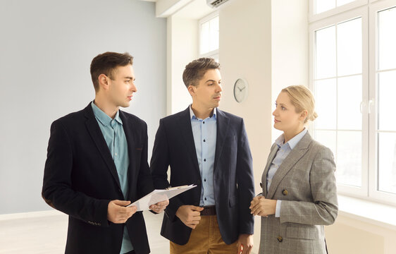 Realtor agent guides couple through apartment showing. They meet in a bright interior, review docs and discuss viewing options with clients and buyers. Clear concept of real estate consultation.
