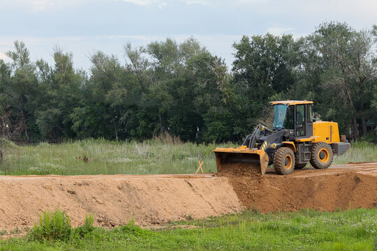 Yellow Front Loader Working on a Dirt Road in a Green Outdoor Landscape