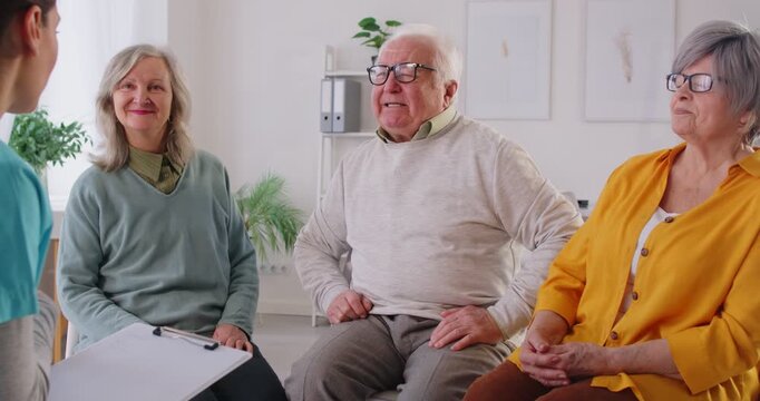 Group of senior people in retirement home having conversation with nurse or doctor. Happy smiling old male and female patients talking to medical worker with clipboard. Senior health care concept