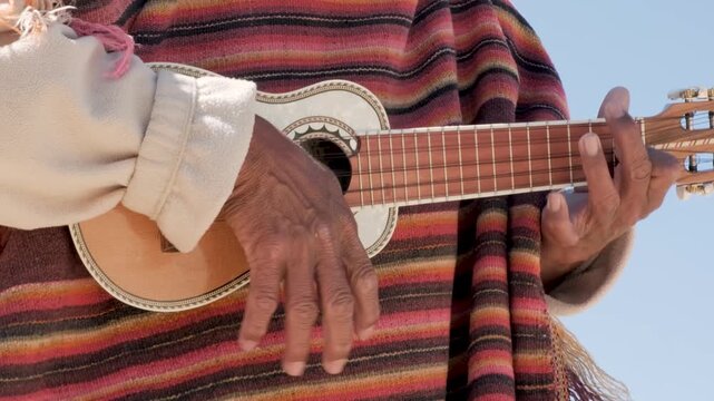 An elderly Aymara musician playing a charango with strings - concept of music