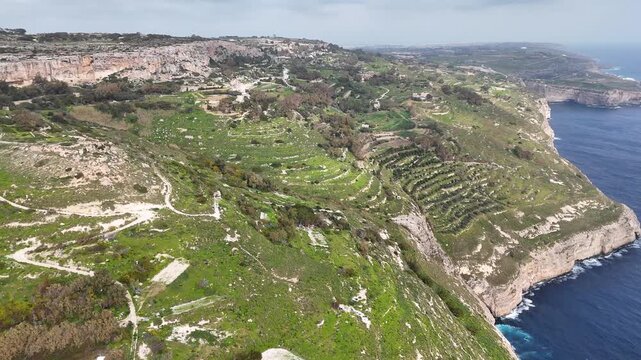 limestone sea cliffs plunge toward the mediterranean beside stepped farmland terraces on maltas rugged west coast dirt trails winding through wild scrubland drystone walls under an overcast sky