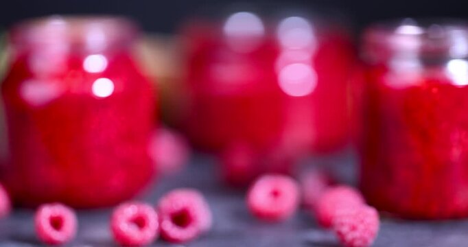   raspberry jam of a rich red hue, the prepared jam in a jar is surrounded by raspberry berries on a black background of the table